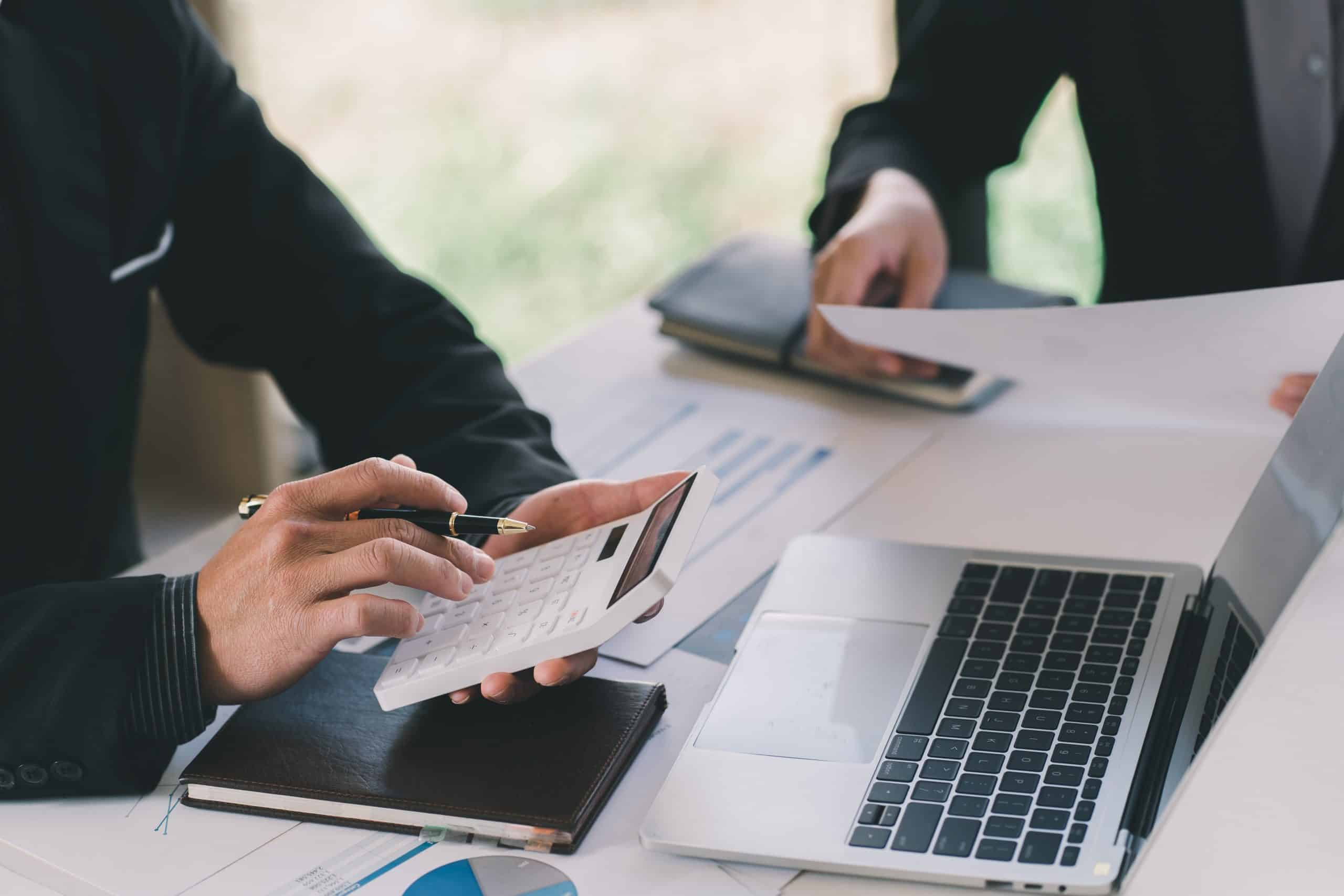 accountant using a white calculator with macbook in background